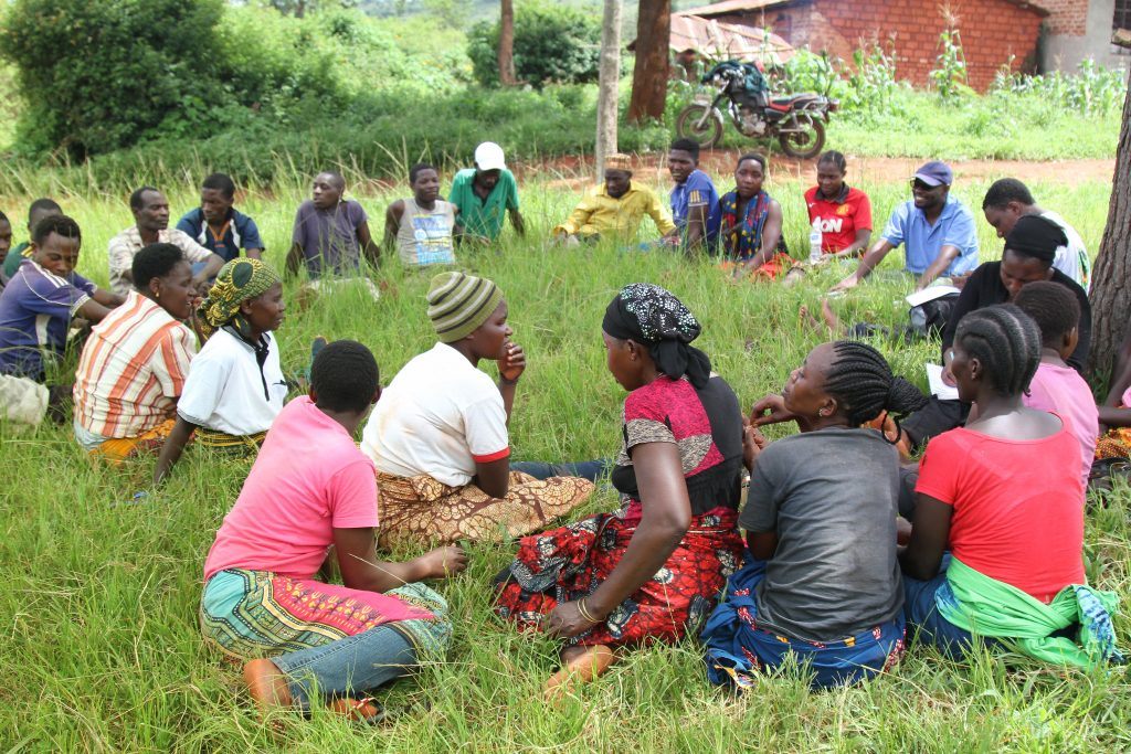 Group of people gathered in the grass in a circle participating in a group discussion in Tanzania.